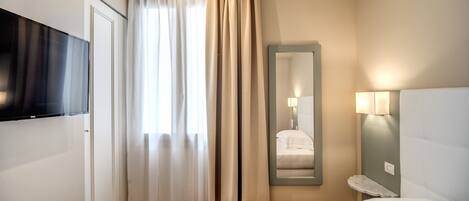 Une chambre d’hôtel équipée d’un lit, d’un téléviseur fixé au mur, d’un miroir et d’une lampe de chevet.