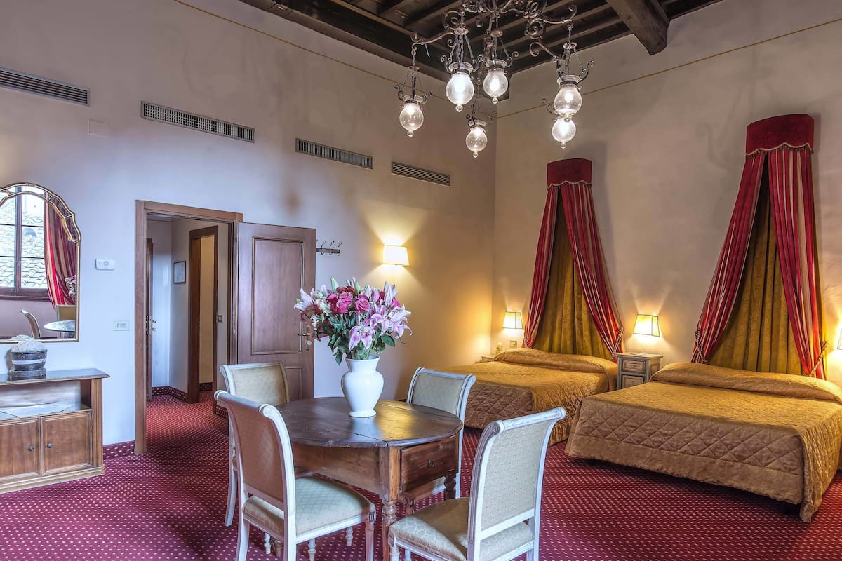 Une chambre d’hôtel avec une table à manger, deux lits, un lustre et un vase de fleurs.
