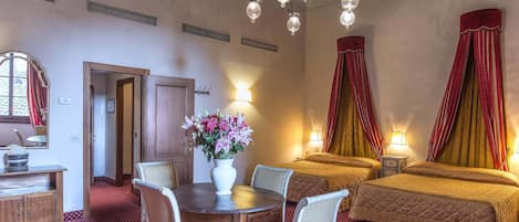 Una habitación de hotel con una mesa de comedor, dos camas, una araña y un florero.