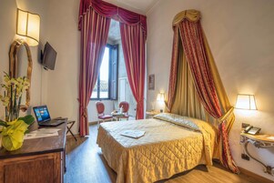 Habitación de hotel con cama, escritorio, ordenador portátil, silla y cortinas.
