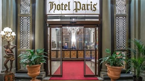 L’entrée de l’hôtel Paris se distingue par son tapis rouge, ses éléments de ferronnerie décoratifs et un réceptionniste derrière le comptoir.