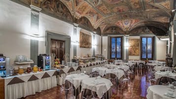A banquet hall with round tables, clear chairs, and a ceiling with frescoes.