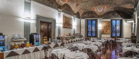 A banquet hall with round tables, clear chairs, and a ceiling with frescoes.