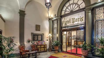 Un'hall con tappeto rosso, una reception e un'ampia finestra ad arco con il cartello "Hotel Paris".
