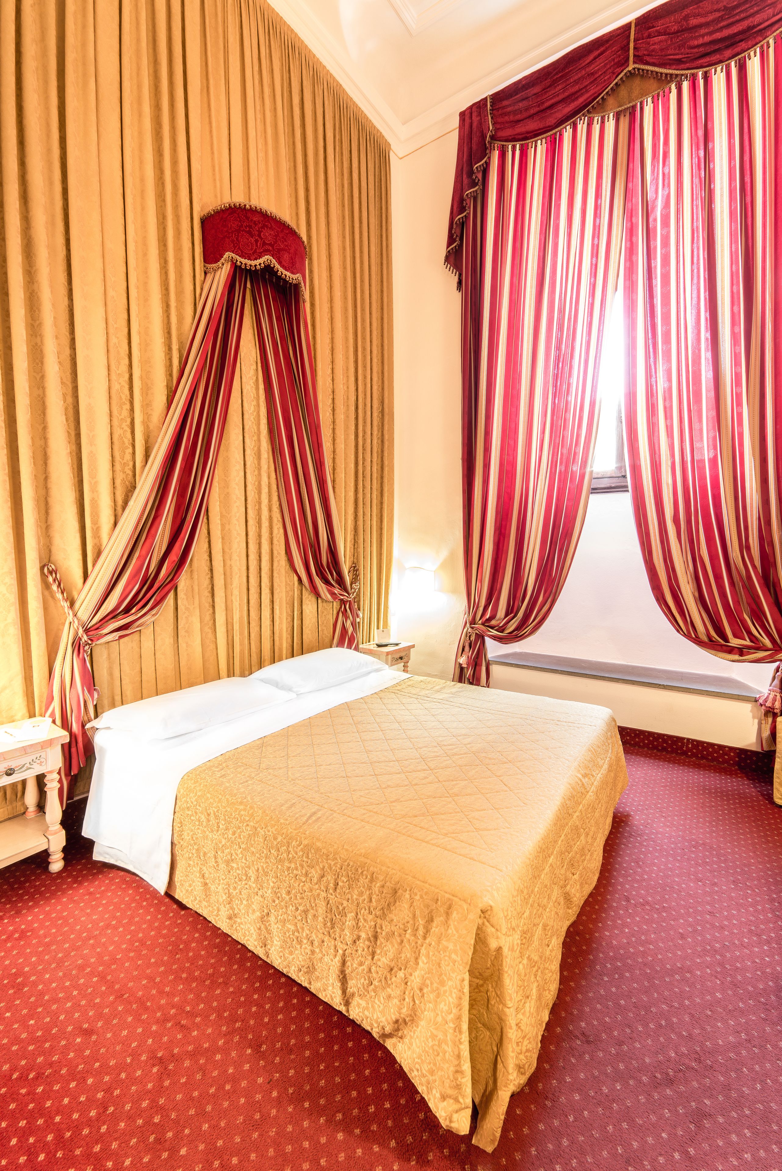 A hotel room with a large bed, a window with curtains, and a red carpeted floor.