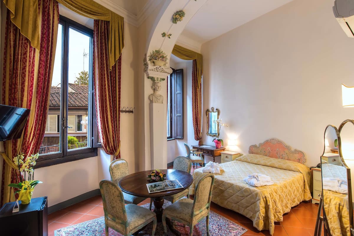 Une chambre d’hôtel avec un lit, un bureau et une chaise, une télévision et une fenêtre avec des rideaux.