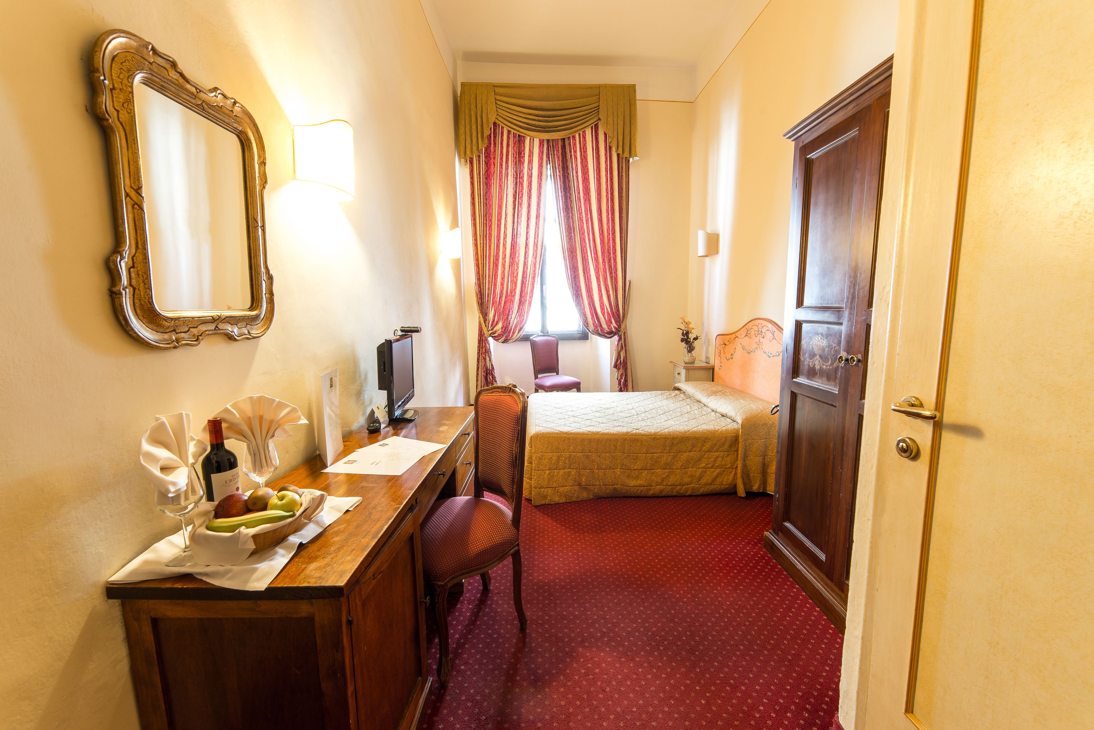 Een hotelkamer met een bed, een bureau met spiegel, een stoel, een dressoir en een raam met gordijnen.