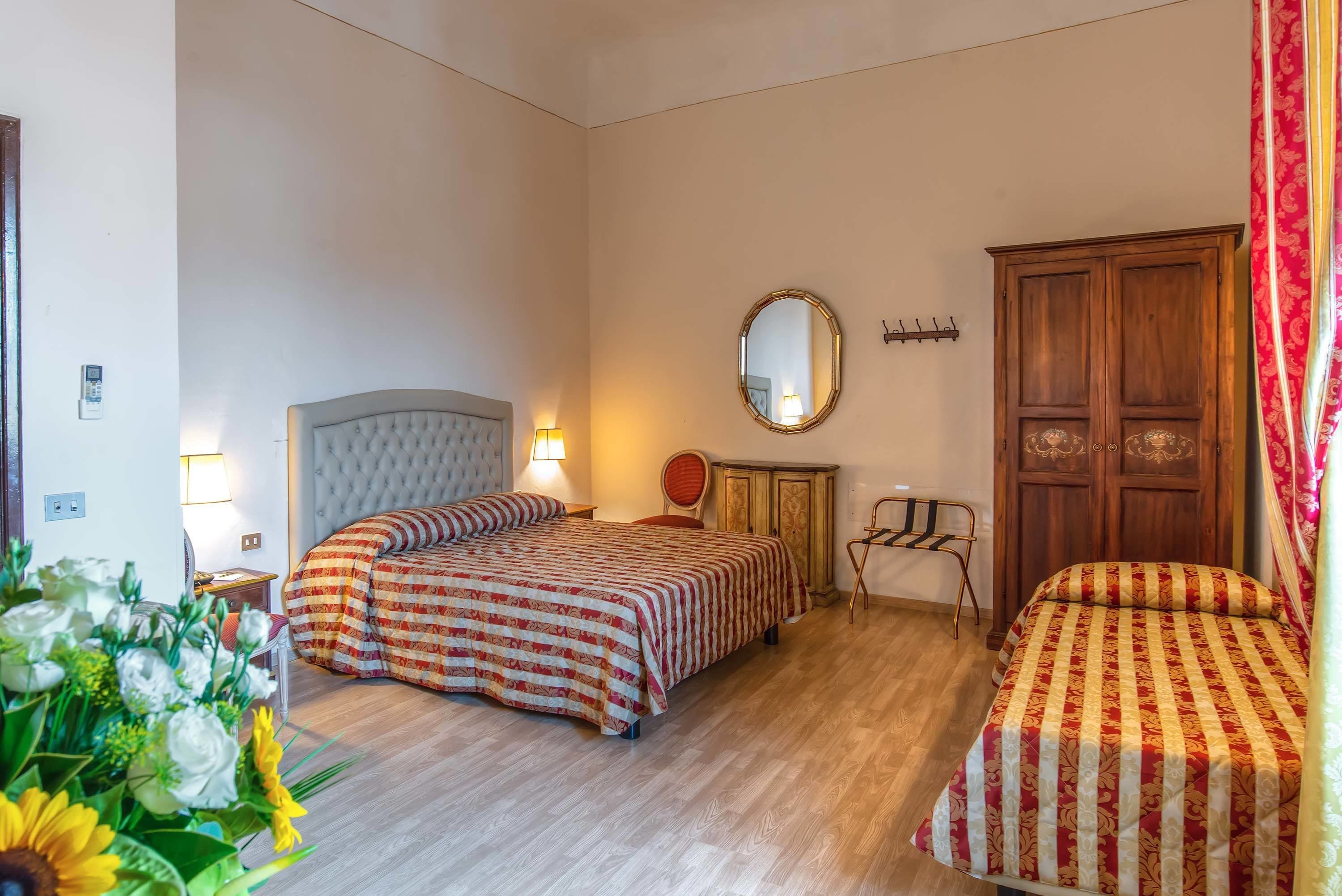 A hotel room with two beds, a wooden wardrobe, a mirror, and a small table with a chair.