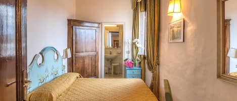 A bedroom with a bed, a nightstand, a dresser, a mirror, and a door leading to a bathroom.