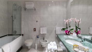 Um banheiro moderno com chuveiro em cabine de vidro, vaso sanitário, bidê, pia com artigos de higiene pessoal e orquídeas decorativas.