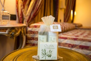 Camera d'albergo con un letto, tende e un tavolo con una bottiglia di sapone all'olio d'oliva.