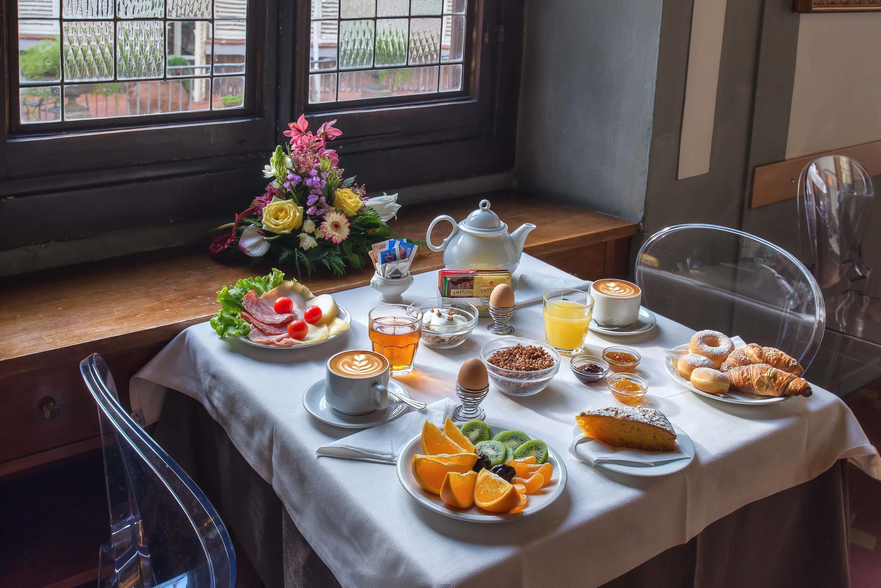 Una mesa de desayuno con diversos alimentos, una tetera y un arreglo floral.