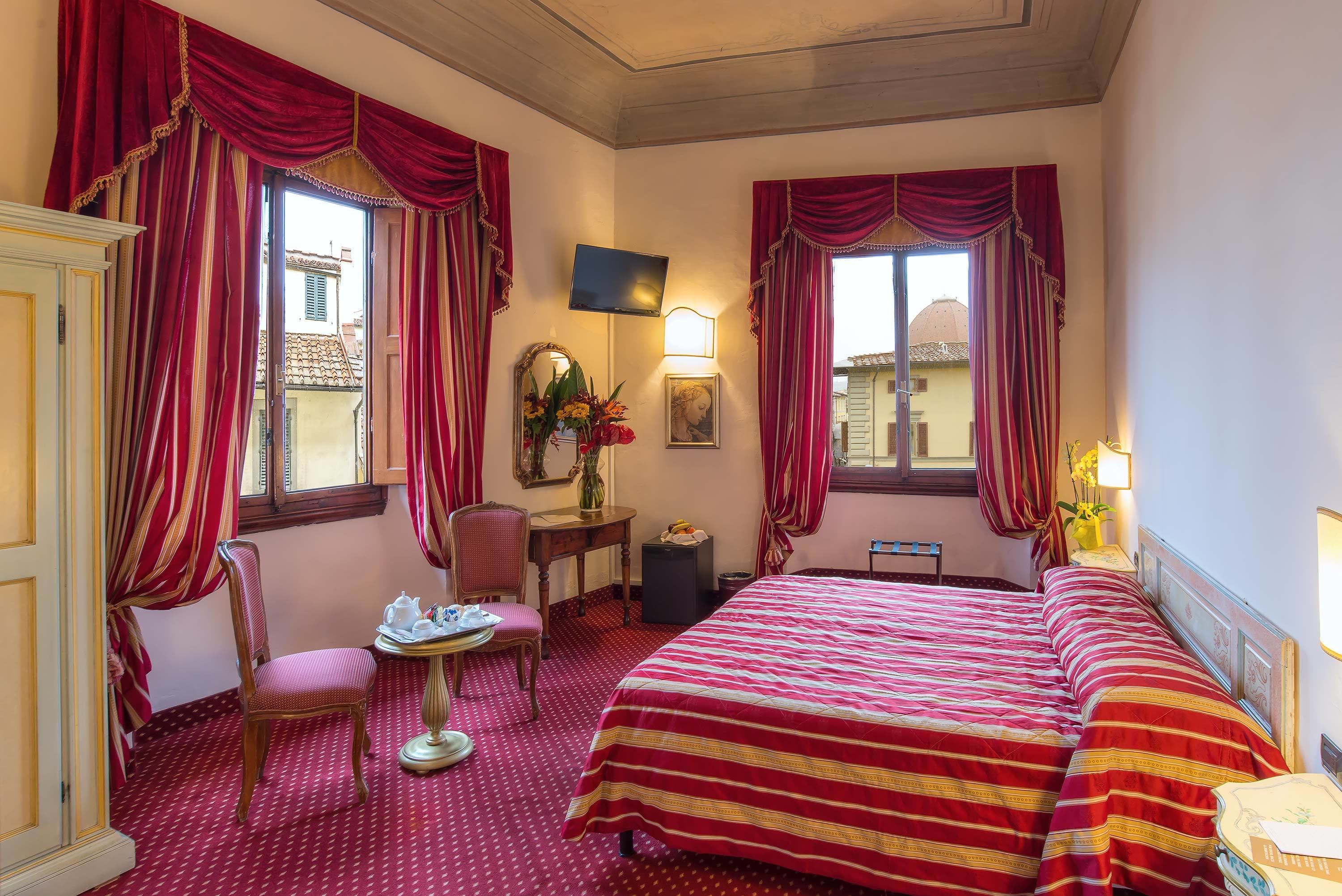 Una habitación de hotel con cama, una silla, una mesa, un espejo y una ventana con cortinas.