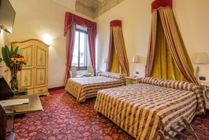 Camera d'albergo con due letti, una scrivania, una sedia, un armadio e una finestra con tende.