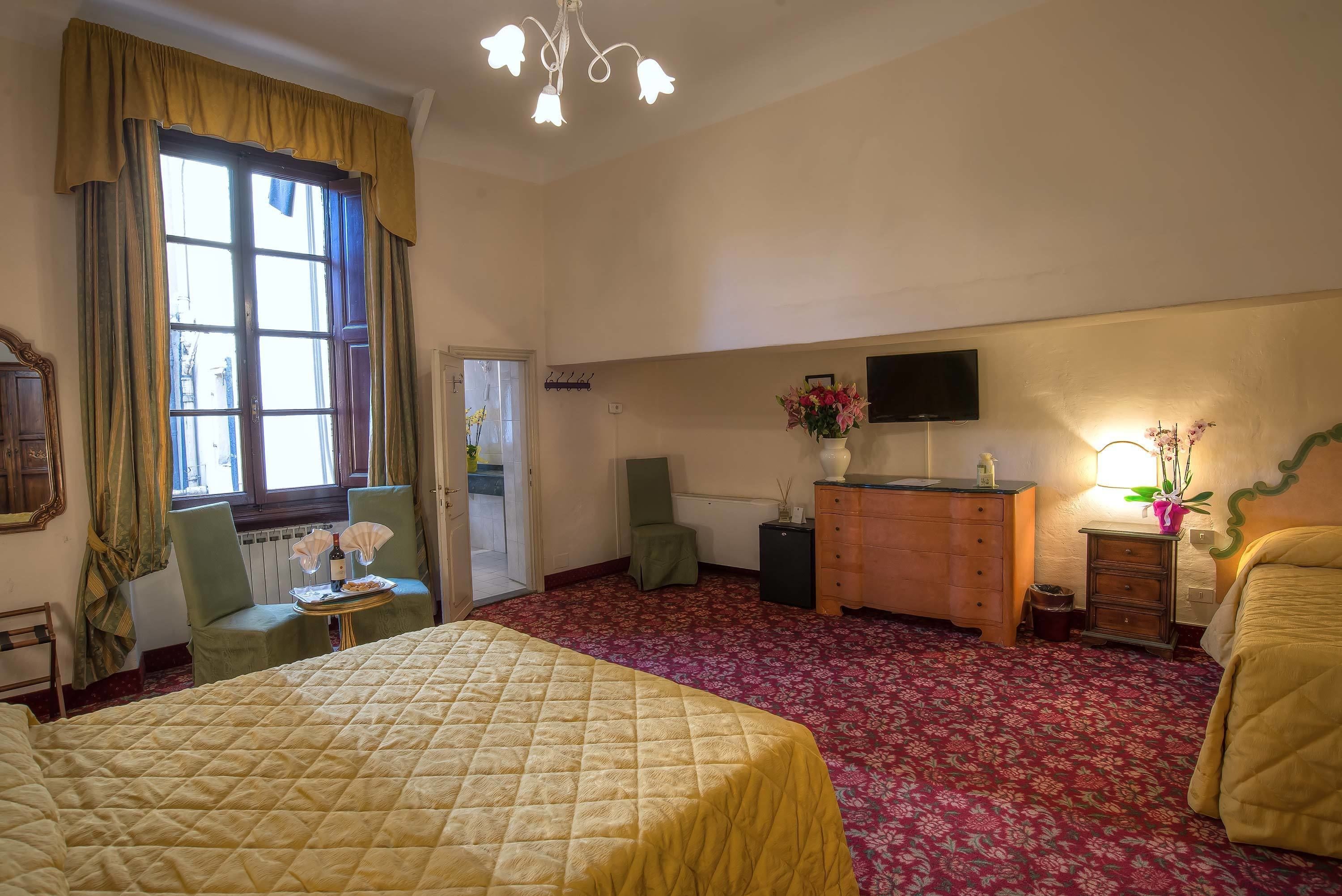 Habitación de hotel con una cama grande, televisión, cómoda y ventana con cortinas.