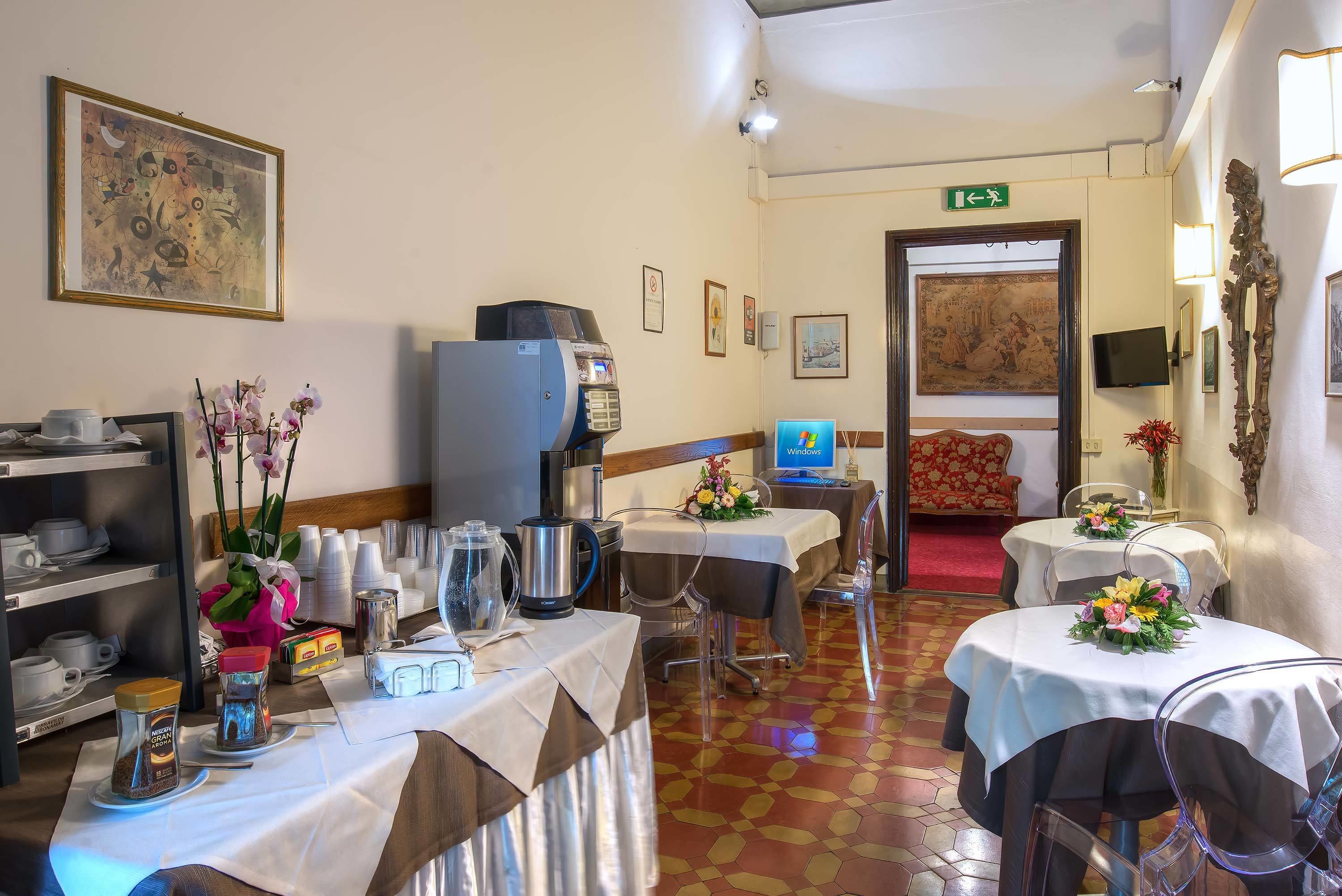 Un comedor de hotel con mesas dispuestas para el servicio, una máquina de café y un cuadro grande en la pared.