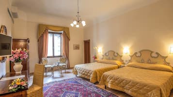 Habitación de hotel con dos camas, un escritorio con un florero, una silla, una ventana con cortinas y una araña.