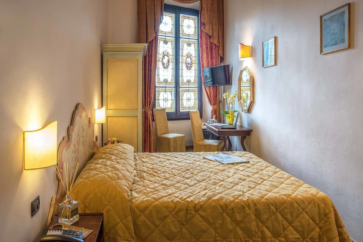 Une chambre d’hôtel avec un lit, un bureau, une chaise, une télévision et une fenêtre avec des rideaux.