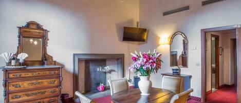 Un área de comedor con una mesa de madera, sillas, una chimenea, un televisor montado en la pared y un espejo en la pared.
