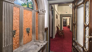Un vaste hall d’entrée orné de colonnes richement décorées, un tapis rouge et une vue sur une pièce illuminée par un lustre.