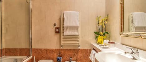 A bathroom with a glass-enclosed shower, a bidet, a sink, and a mirror.