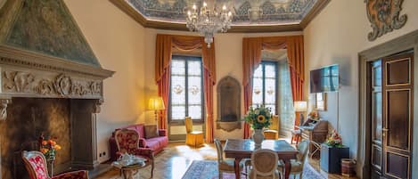 A grand room with a fireplace, ornate ceiling, and a chandelier.