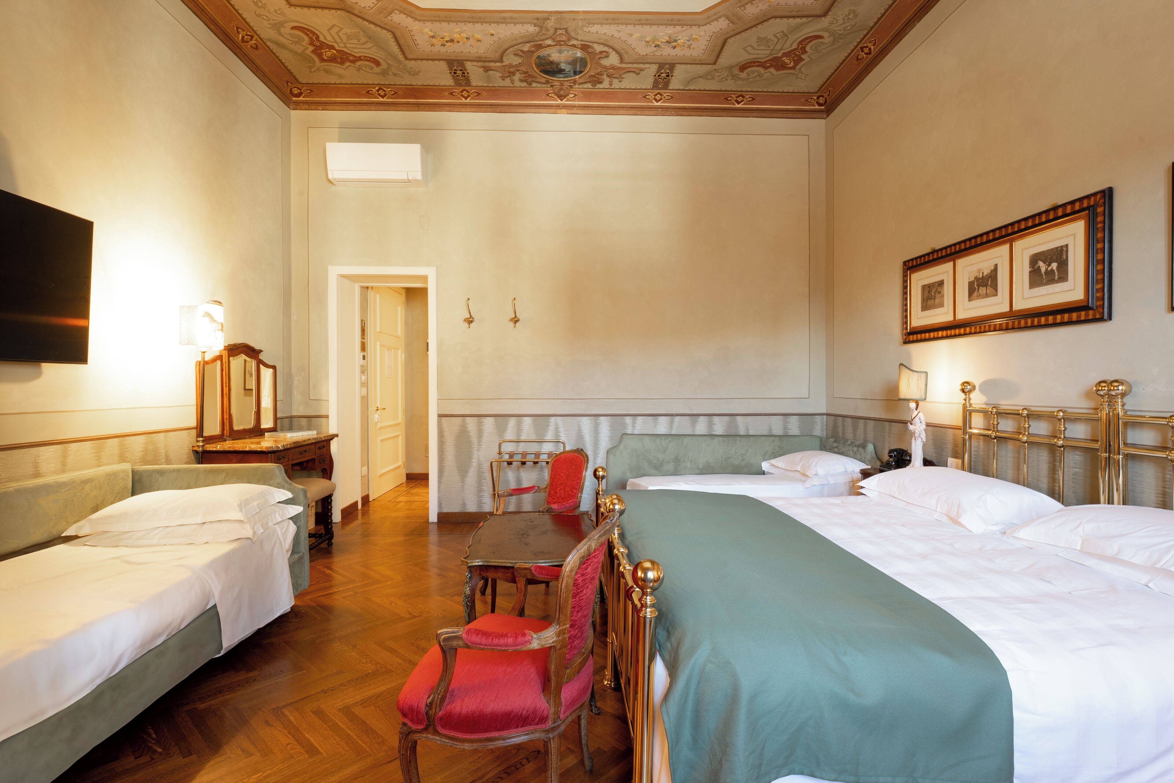A hotel room with two single beds, a wooden desk with a chair, a small table with a chair, and a television on the wall.