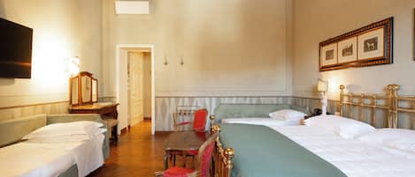 A hotel room with two single beds, a wooden desk with a chair, a small table with a chair, and a television on the wall.