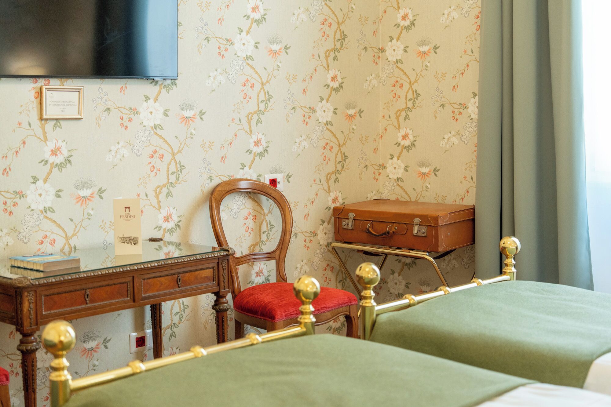 Une chambre avec deux lits, un bureau en bois, une chaise, une valise et un téléviseur fixé au mur.
