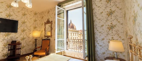 Habitación de hotel con cama, escritorio, silla, televisión y ventana con vista a un edificio.