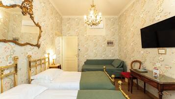 Una habitación de hotel con dos camas, un sofá verde, un escritorio de madera y un candelabro.