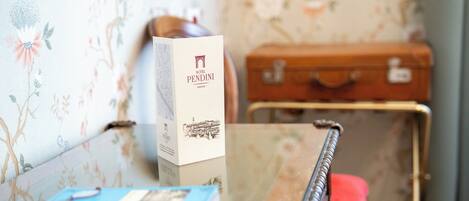 A hotel room with a wooden table, a blue notebook, a white box labeled 'PENDINI HOTEL FERRAZE', and a vintage suitcase.