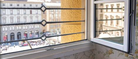 A window with a view of a historic building, a wooden ledge with a book, a cup of coffee, and a teapot.