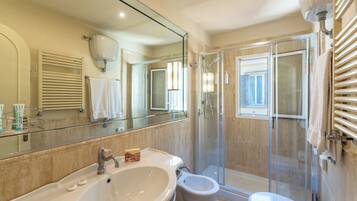 A modern bathroom with a large mirror, a sink, a bidet, and a glass-enclosed shower.
