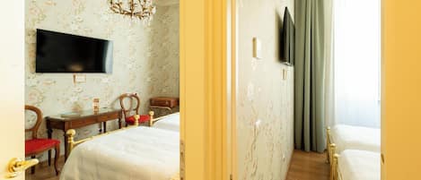A hotel room with two beds, a television, a desk with a chair, and a chandelier.