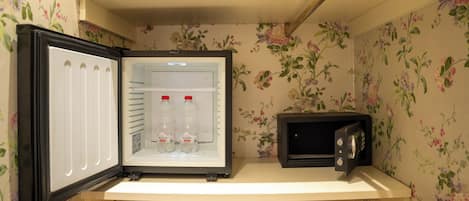 A compact refrigerator with a freezer compartment, a microwave, and a shelf with two bottles of Alisea water.
