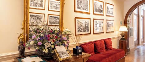 A lobby with a red sofa, a wooden console table with a vase of flowers, a large mirror, and framed black and white photographs on the wall.