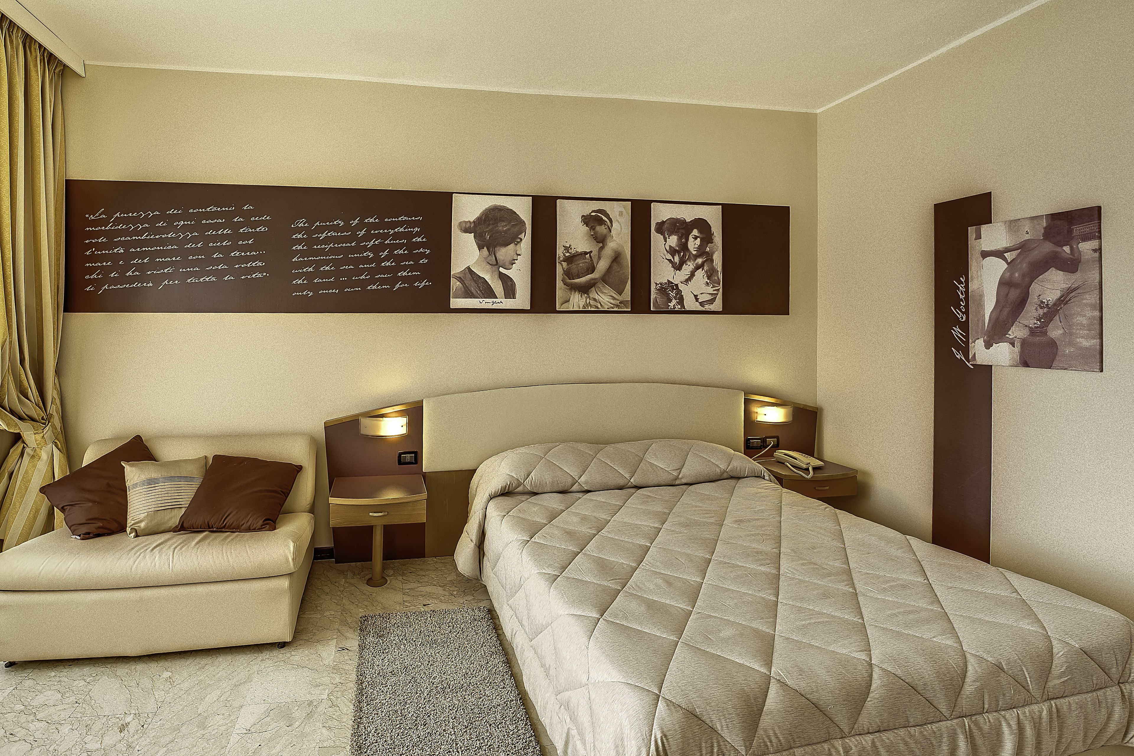 Une chambre d’hôtel avec un lit, un canapé, une table de chevet et un mur orné de tableaux.