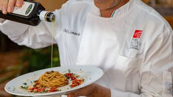Un chef con uniforme blanco sirviendo salsa sobre una porción de espagueti.