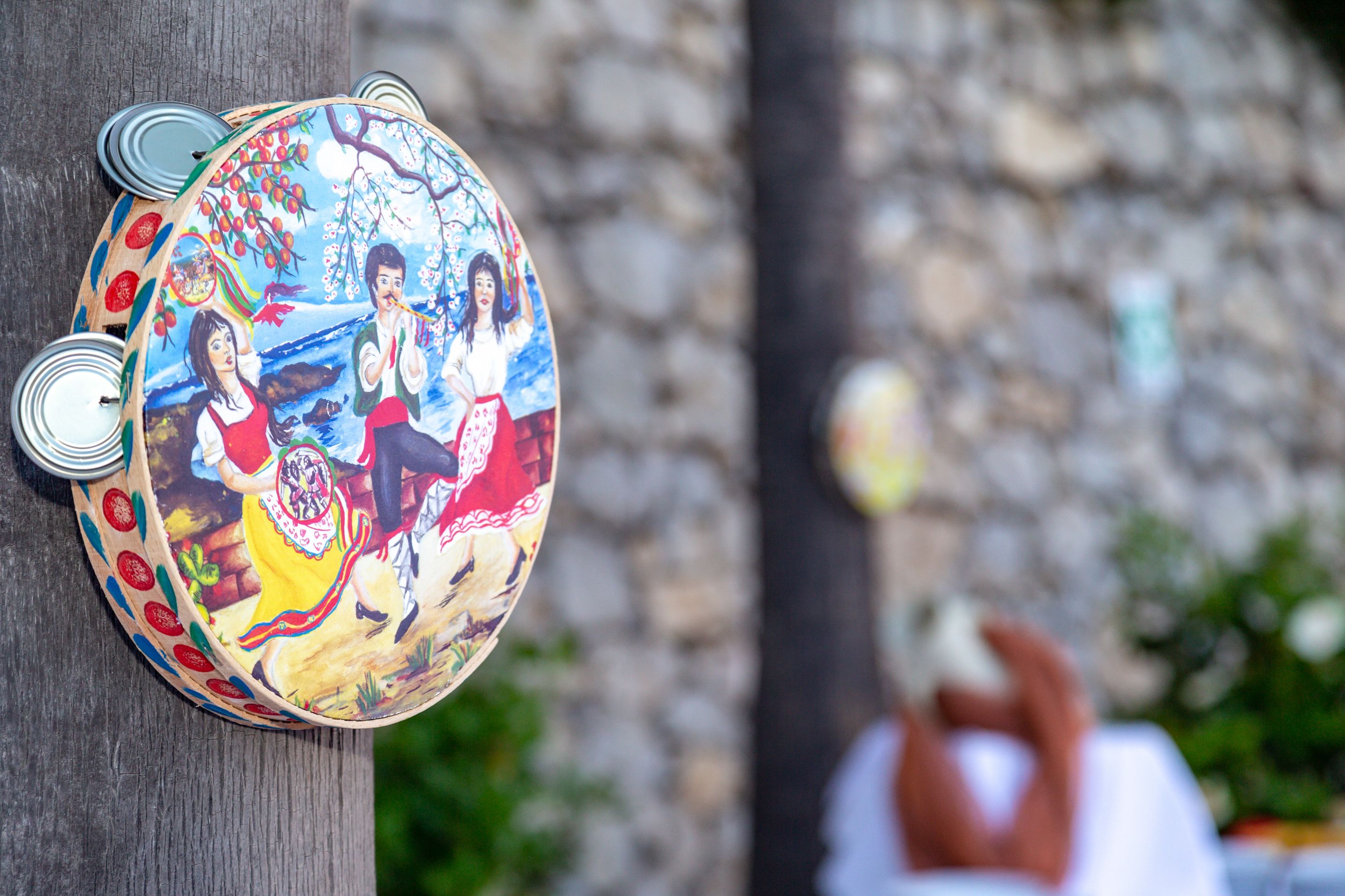 A colorful, hand-painted wooden object with a scene of people and nature, mounted on a wooden post.