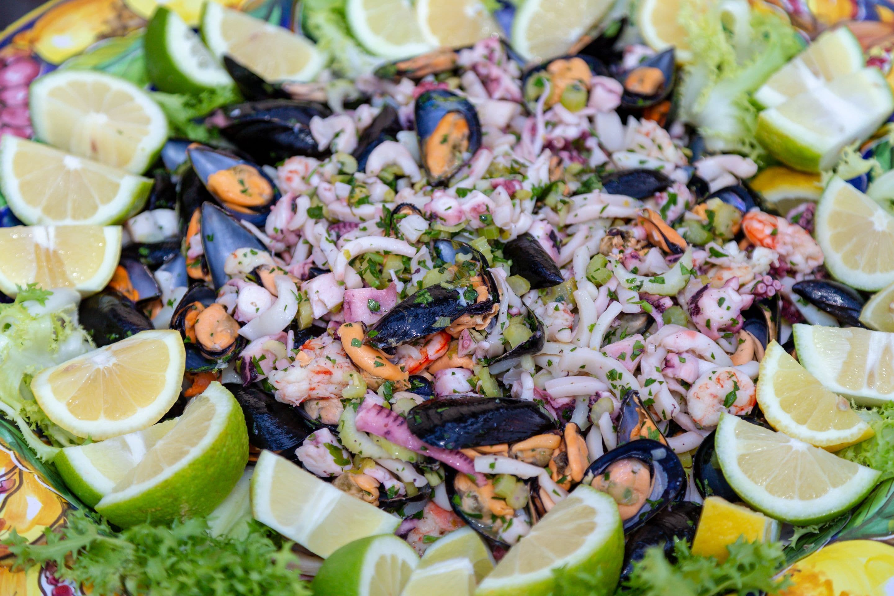 Une salade de fruits de mer comprenant différents types de fruits de mer, notamment des crevettes, des moules et du calmar, et agrémentée d’herbes et de tranches de citron vert.