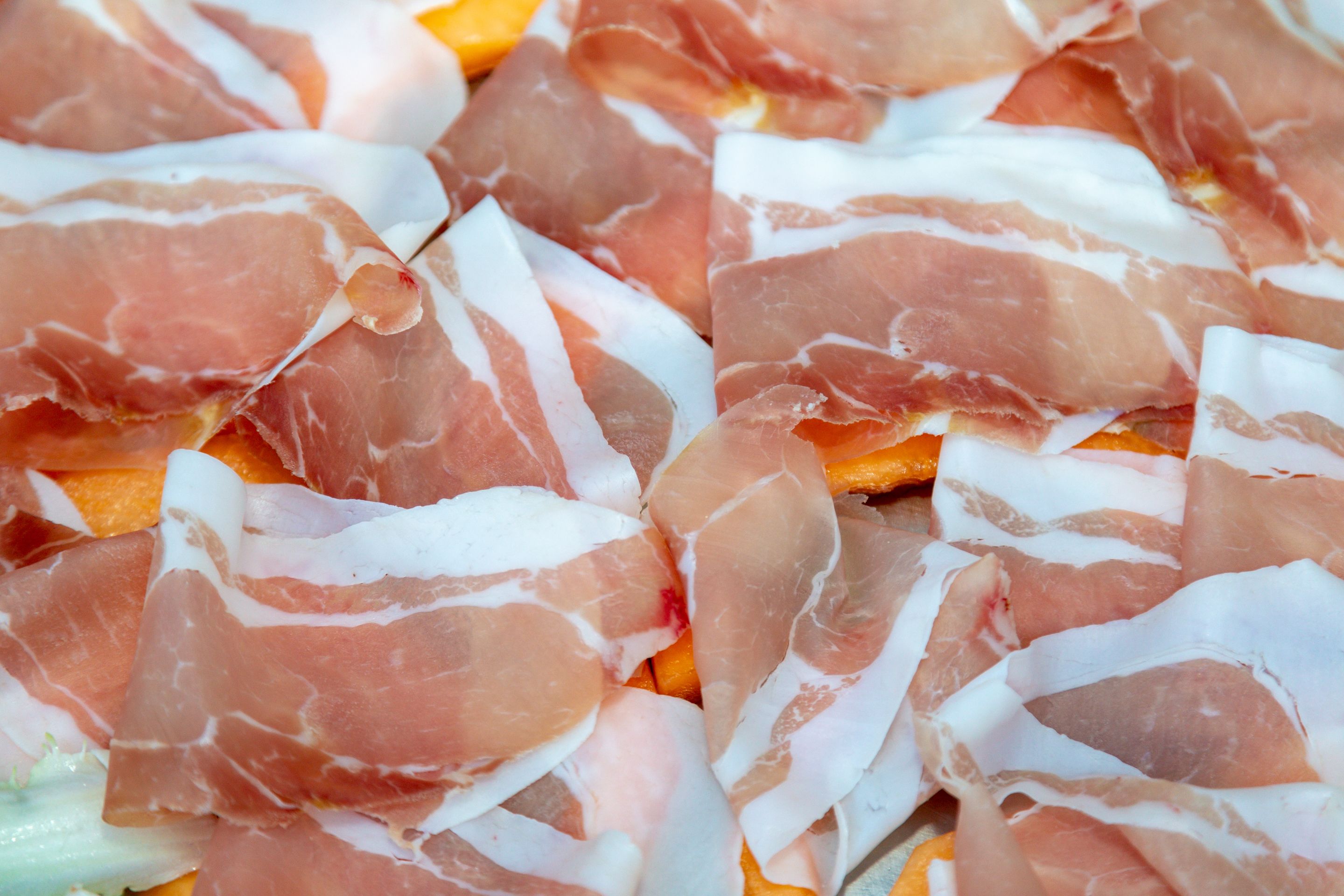 Ein Detailbild von dünn geschnittenem, geköbtem Fleisch, vermutlich Prosciutto, auf einer Bettung aus Orangenscheiben.