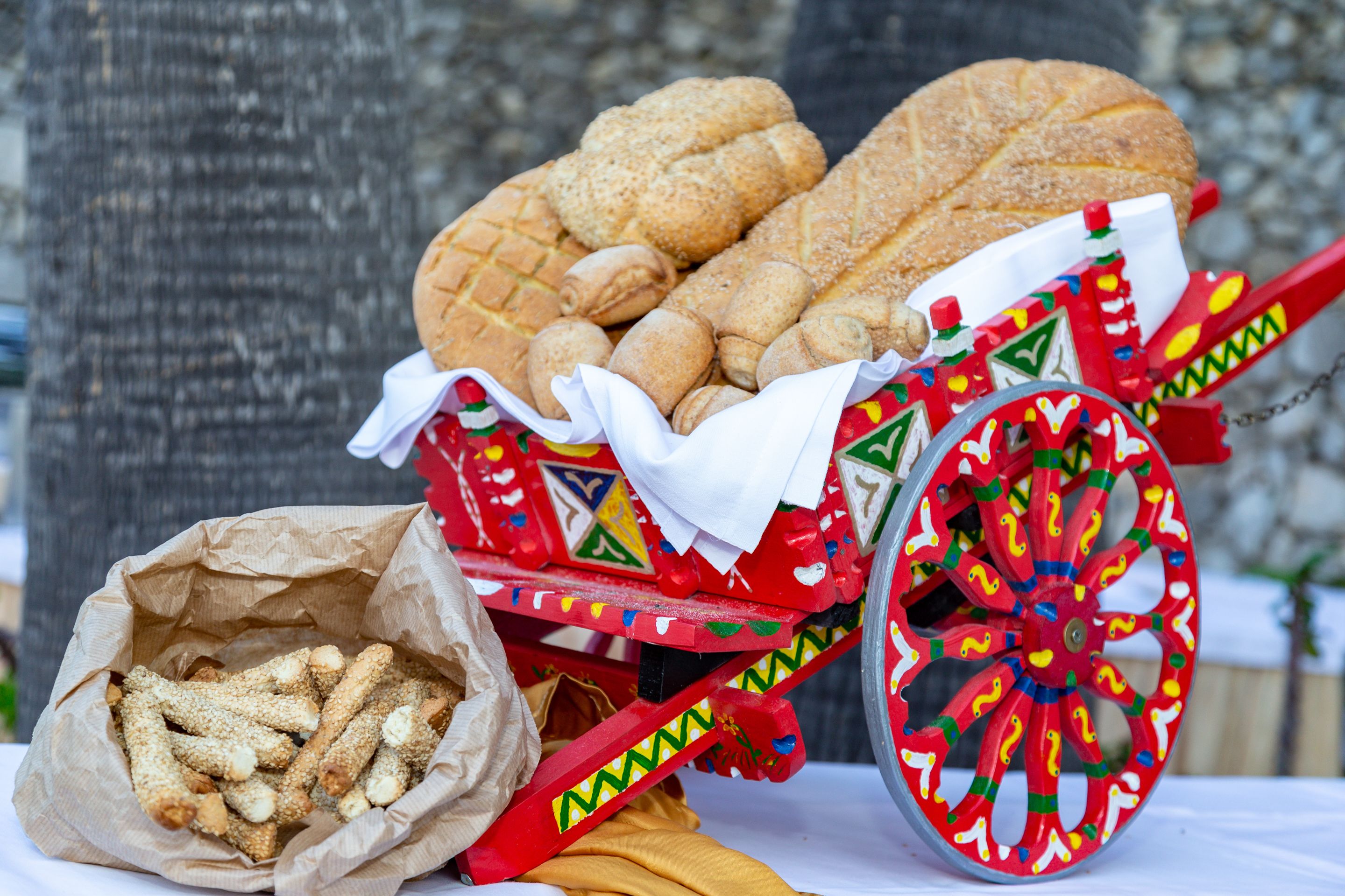Un chariot coloré rempli de différents types de pain et de viennoiseries, un sac de gressins et une roue décorative.