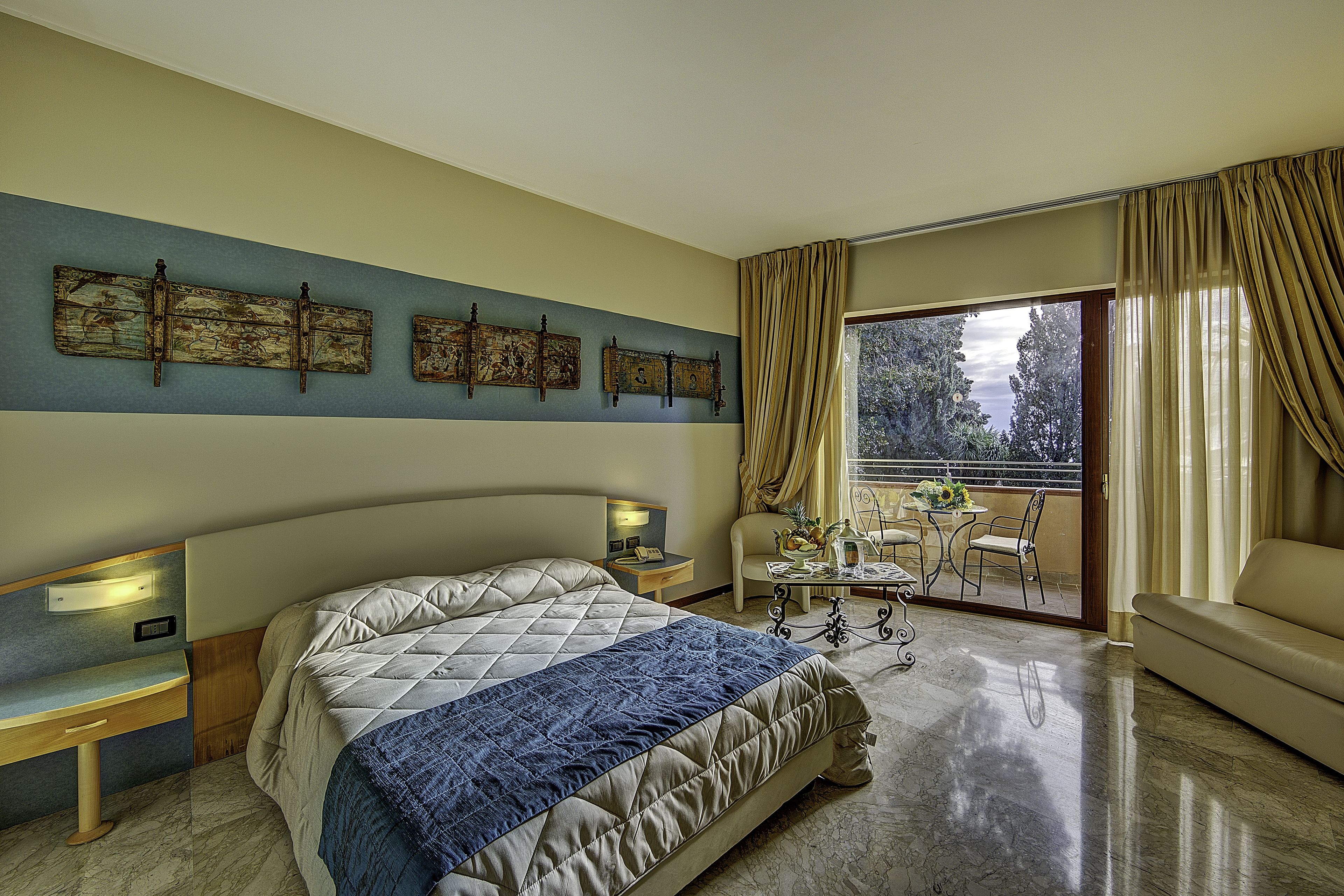Une chambre à coucher comprenant un lit, des tables de chevet, un bureau, une chaise, un canapé et un balcon avec vue.