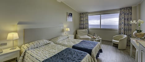 Habitación de hotel con dos camas, un escritorio, una silla y vistas al cielo a través de la ventana.