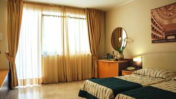 Une chambre d’hôtel avec deux lits, une table de chevet en bois avec une lampe, un miroir et un tableau encadré au mur.