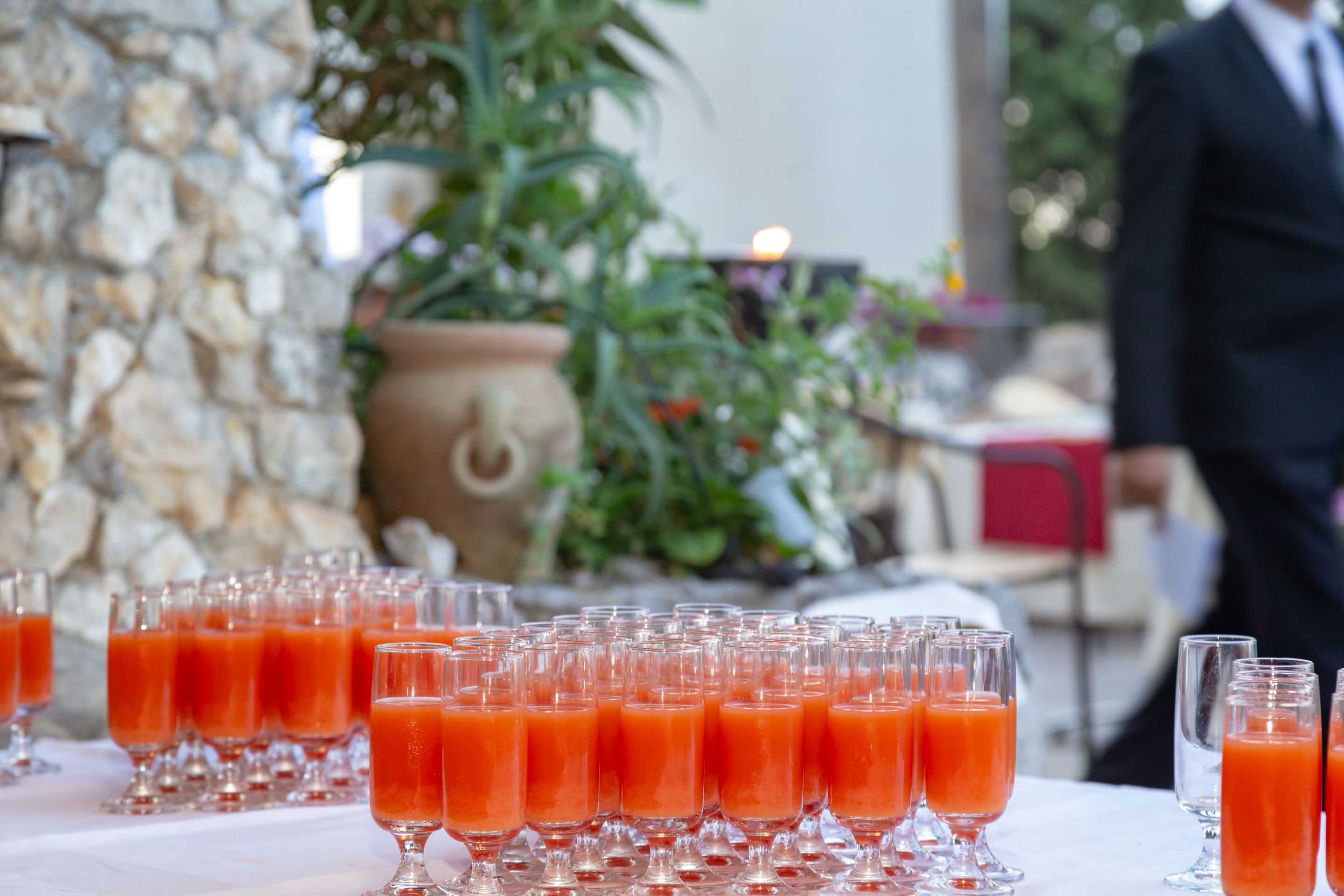A table with multiple glasses of orange juice, a stone wall, and a potted plant in the background.