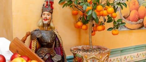 A statue of a knight with a helmet and armor, a potted orange tree, and a bowl of apples.