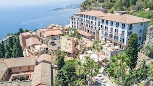 Un hotel frente al mar, con varios pisos, balcones con plantas y vistas al océano.