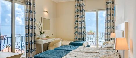 A hotel room with two beds, a desk, a chair, and a balcony with a railing.